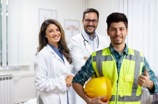 Médica, médico e trabalhador com colete e capacete sorrindo em um consultório