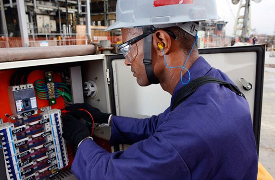 Eletricista com capacete e óculos de proteção trabalhando em um painel elétrico