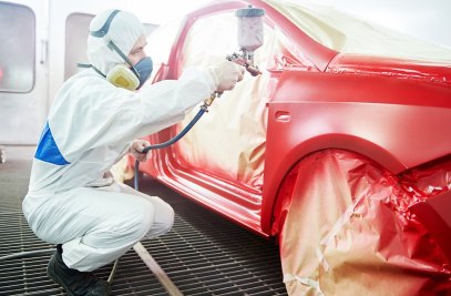 Pintor com macacão e máscara pintando um automóvel